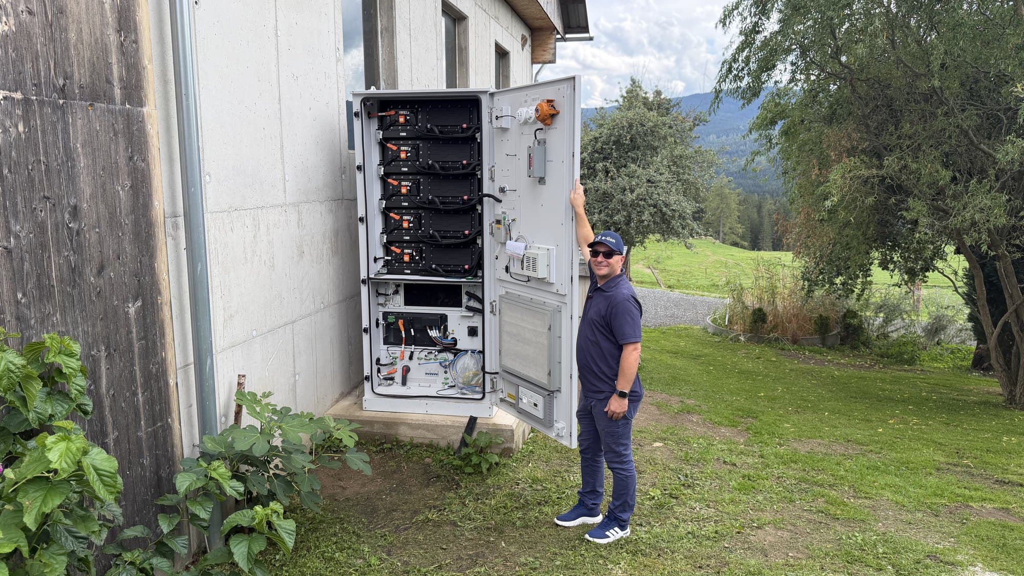 Von e-lion installierter Gewerbespeicher im Außenschrank mit geöffneter Tür, daneben ein Mitarbeiter mit e-lion-Kappe Von e-lion installierter Gewerbespeicher im Außenschrank mit geöffneter Tür, daneben ein Mitarbeiter mit e-lion-Kappe